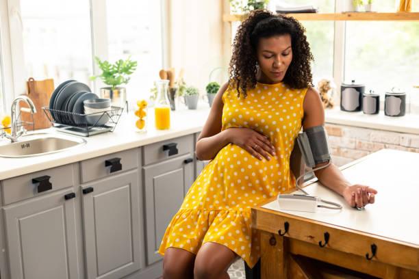Pregnant woman sitting in her kitchen using remote pregnancy monitoring.